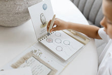 Load image into Gallery viewer, Close-up of a child using the water pen to reveal pastel colors on a page of balloon illustrations.