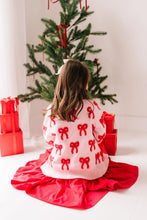 Load image into Gallery viewer, Back view of a seated child wearing the blush pink cardigan, showing allover red bows and a wide ribbed hem.