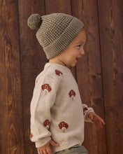 Load image into Gallery viewer, Side close-up of a child wearing a cream sweater with reddish-brown mushroom motifs and ribbed cuffs and hem.