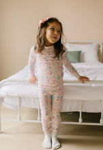 Load image into Gallery viewer, Full-length front view of a child wearing the Sugar Plum pajama top and matching pants beside a white bed frame.
