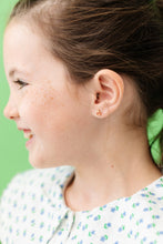 Load image into Gallery viewer, Close-up of a child wearing a red and gold-tone ladybug stud earring against a green background.