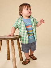 Load image into Gallery viewer, Child wearing a green checkered shirt over a blue graphic t-shirt, standing next to a wooden stool on a beige background.