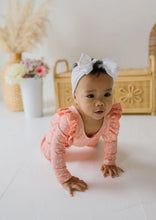 Load image into Gallery viewer, A baby crawling on a white floor wearing a peach long-sleeve romper with white polka dots and a white bow headband, with a soft-focus nursery background.