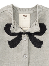 Load image into Gallery viewer, Close-up of a light gray knit cardigan sweater with a large black bow motif across the chest and a cream neck label reading tea.