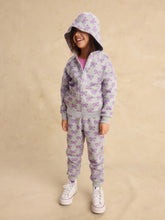 Load image into Gallery viewer, A young child wearing a light gray zip-up hoodie and matching jogger pants set, both covered in a purple bow pattern, standing against a textured beige studio backdrop.