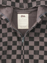 Load image into Gallery viewer, Close-up of a zip-front garment with a black and muted taupe-gray checkerboard pattern, showing the inner collar and a white sewn-in label that reads 'tea'.