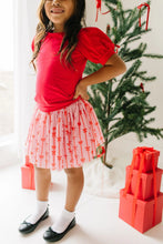 Load image into Gallery viewer, Child wearing a pink Dainty Bows tulle skirt with a red top, white socks, and black ballet flats beside a Christmas tree.
