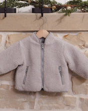 Load image into Gallery viewer, Fog gray shearling jacket hanging against a stone fireplace, showing the front zipper and two zippered pockets.