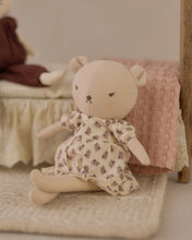 Load image into Gallery viewer, Bonnie the Bear seated beside a miniature bed with a pink blanket, wearing her cream floral dress.
