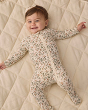 Load image into Gallery viewer, Smiling baby lying with arms outstretched in a cream floral zip footie on a quilted blanket.