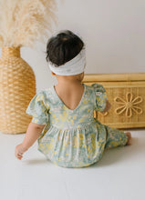 Load image into Gallery viewer, Baby in a floral romper standing in front of a woven basket.
