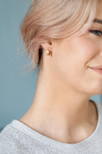 Load image into Gallery viewer, Close-up of a person wearing a gold-tone daisy hoop earring against a muted blue background.