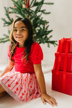 Load image into Gallery viewer, Closer view of a seated child wearing the pink tulle skirt, showing red bows, vertical stripes, and a sheer pink hem.
