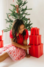 Load image into Gallery viewer, Child seated beside stacked red gifts in a pink bow-print tulle skirt and red puff-sleeve top.