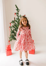 Load image into Gallery viewer, Front view of a child wearing the pink Dainty Bows dress with hands in its side pockets beside a Christmas tree.