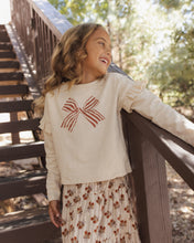 Load image into Gallery viewer, Ruffle Long Sleeve Tee in Bow, cream on a girl on outdoor stairs