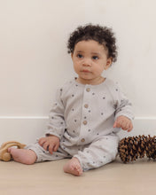 Load image into Gallery viewer, A baby with curly dark hair sits on a light wood floor wearing a light gray waffle-knit romper with small dark star prints and wooden buttons. A wooden toy is on the left, and a pinecone is on the right, against a plain off-white wall.