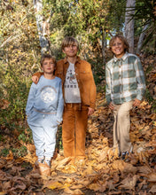 Load image into Gallery viewer, Three boys standing together outdoors on a ground covered in fallen leaves, wearing casual autumn clothing. The boy in the center wears a brown jacket and matching brown pants over a graphic T-shirt, the boy on the left wears a light blue sweatshirt and sweatpants, and the boy on the right wears a green plaid shirt and beige pants.