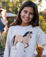 Load image into Gallery viewer, A young girl smiling while wearing a light gray knit sweater with a large horse graphic in tan, brown, and black on the front, photographed outdoors with a blurred background.