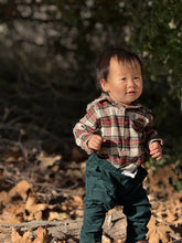 Load image into Gallery viewer, A toddler standing outdoors on a bed of dry leaves, wearing a beige and red plaid long-sleeve button-up shirt with dark green pants.