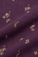 Load image into Gallery viewer, A close-up of a knitted fabric in deep plum purple, featuring a delicate scattered pattern of small floral motifs in muted yellow, pink, and green.