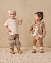 Load image into Gallery viewer, Two toddlers modeling coordinated neutral-toned clothing in a softly lit indoor studio setting. The child on the left wears a cream short-sleeve top with small animal motifs, tan pants, and tan shoes.