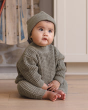 Load image into Gallery viewer, Baby sitting on a wooden floor wearing spruce green chunky knit pants with a matching sweater and knit hat.