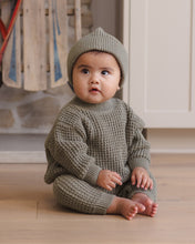Load image into Gallery viewer, Front view of a seated baby wearing spruce green chunky knit pants with ribbed cuffs, a matching sweater, and knit hat.