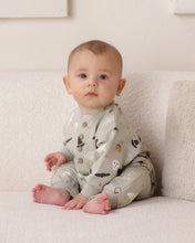 Load image into Gallery viewer, A baby sitting on a textured cream couch wearing a light gray long-sleeve pajama set with a Halloween print of ghosts, bats, and witches.