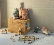 Load image into Gallery viewer, Wicker toy box with stuffed animals and toys on a light gray floor against a textured wall.