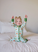 Load image into Gallery viewer, Child wearing a colorful onesie with rainbow patterns, sitting on a bed.