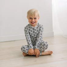 Load image into Gallery viewer, Child wearing a patterned onesie sitting on a wooden floor.