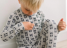 Load image into Gallery viewer, Child wearing a gray onesie with black and white dog pattern on a light background