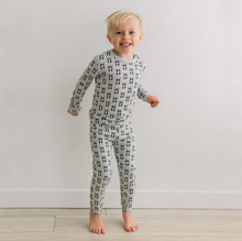 Load image into Gallery viewer, Child wearing a patterned onesie standing on a wooden floor with a white wall background