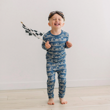 Load image into Gallery viewer, Child wearing blue pajamas with car pattern, holding a checkered flag, on a light wooden floor.