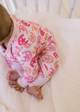 Load image into Gallery viewer, Baby in a crib wearing a pink and orange patterned outfit.