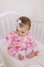 Load image into Gallery viewer, Baby in a pink outfit with horseshoe patterns sitting in a crib.