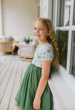 Load image into Gallery viewer, Young girl in a colorful top and green skirt standing on a porch.