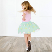 Load image into Gallery viewer, Child wearing a pink top and green skirt on a wooden floor.