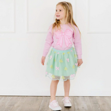 Load image into Gallery viewer, Young girl wearing a pink sweater with a bow and a green skirt on a white background.