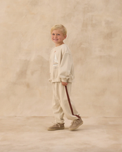 Load image into Gallery viewer, Young boy in a white outfit standing against a beige background