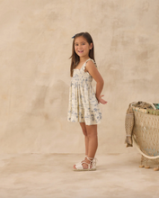 Load image into Gallery viewer, Young girl in a floral dress standing on a beige background
