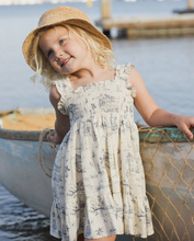 Load image into Gallery viewer, Young girl in a floral dress and straw hat sitting in a small boat by the water.