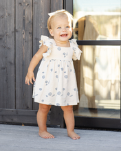 Load image into Gallery viewer, Child wearing a white dress with blue patterns standing on a wooden deck.