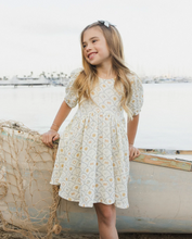 Load image into Gallery viewer, Young girl in a dress standing by a boat on a beach.