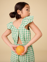 Load image into Gallery viewer, Child wearing a green checkered outfit holding an orange against a beige background