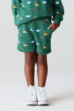 Load image into Gallery viewer, Child wearing a green outfit with animal patterns on a white background