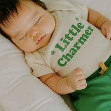 Load image into Gallery viewer, Baby wearing a onesie with 'Little Charmer' text, lying on a white surface.