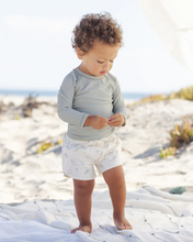 Load image into Gallery viewer, Child in gray long-sleeve shirt and white shorts standing on a sandy beach.
