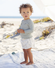 Load image into Gallery viewer, Child standing on a sandy beach wearing a light gray long-sleeve shirt and white shorts with a pattern.